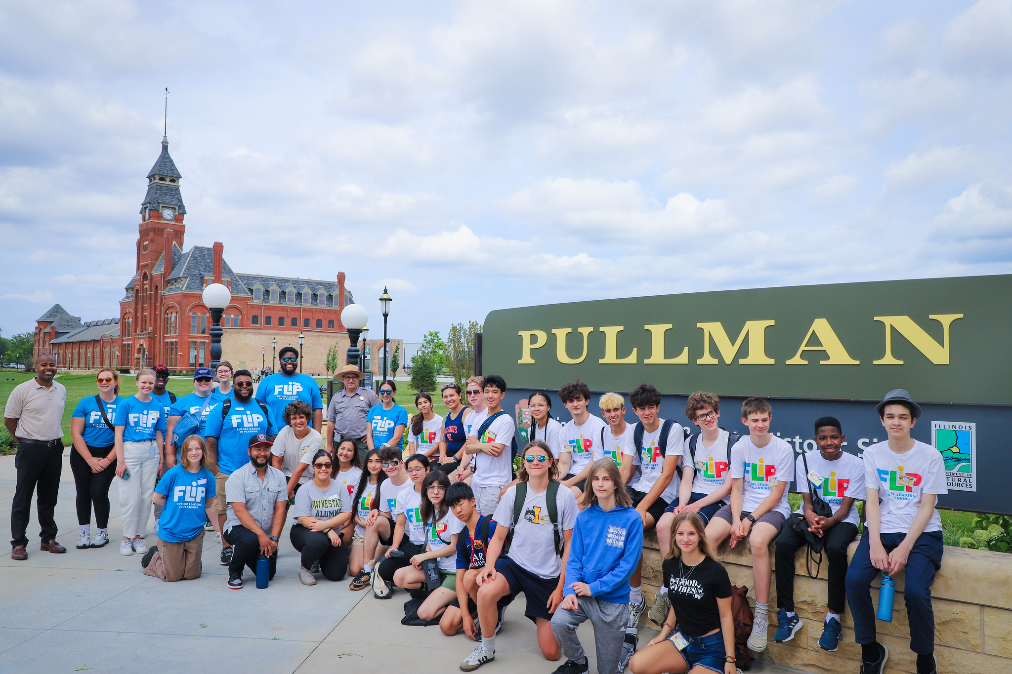 Large group of FLIP students posing in front of a sign that reads, "Pullman" with the Pullman Factory in a distance.