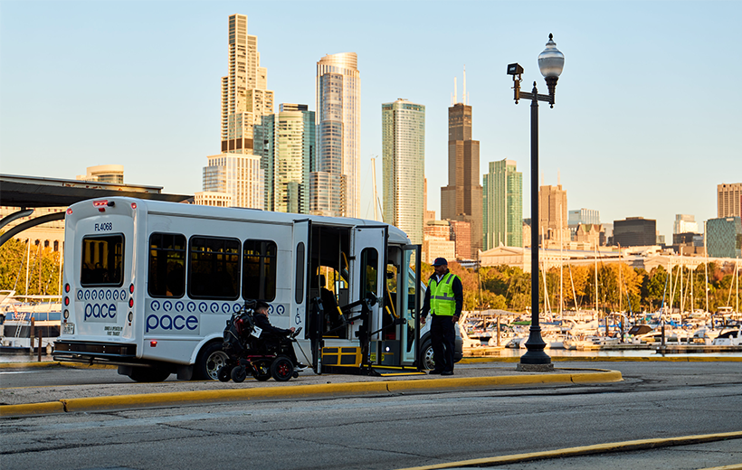 A driver assists a wheelchair user boarding a Pace bus via wheelchair lift