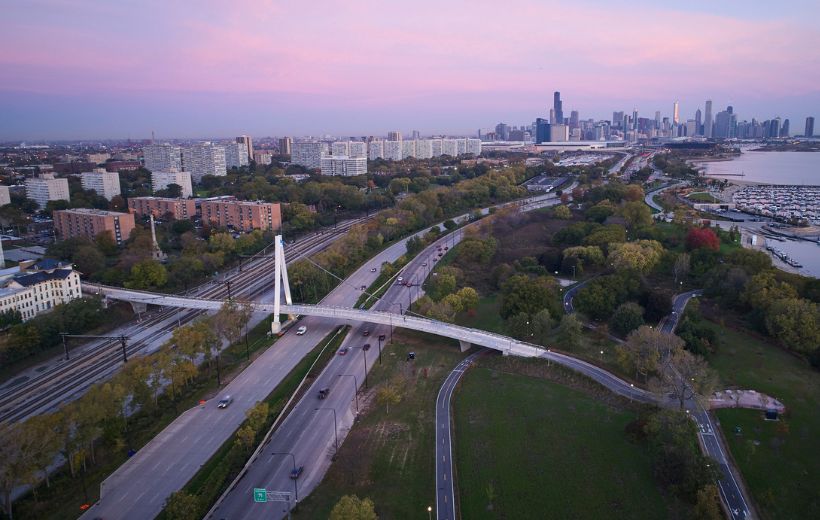 Bridge over bike path, roads, and rails. Chicago skyline in background. Sky is purple from sunset