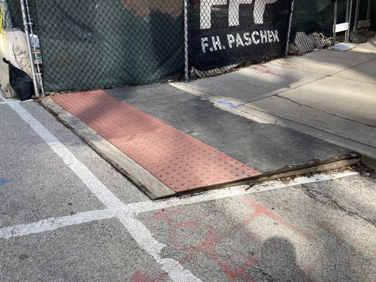 A temporary curb ramp, made of wood, with an orange truncated dome strip (small bumps) at the base.