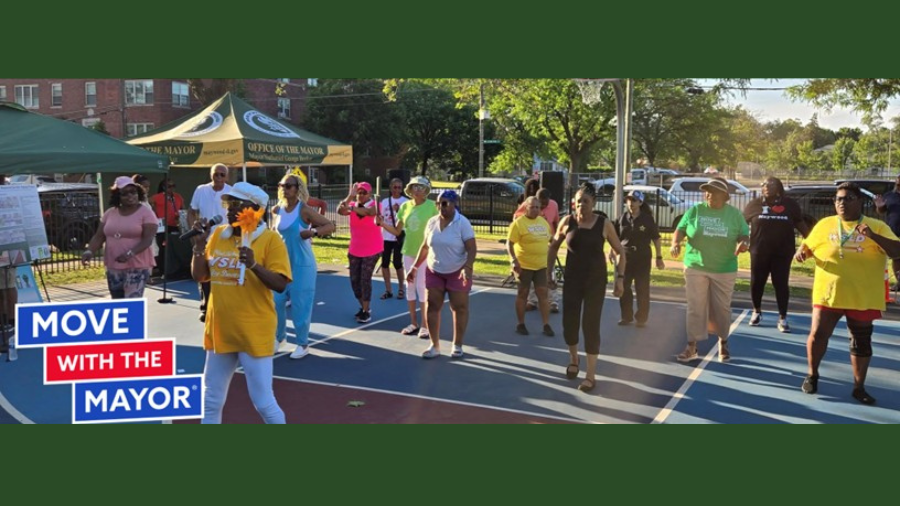 Group of people on a backsetall court. They are following a leader in movement. Logo: Move with the Mayor