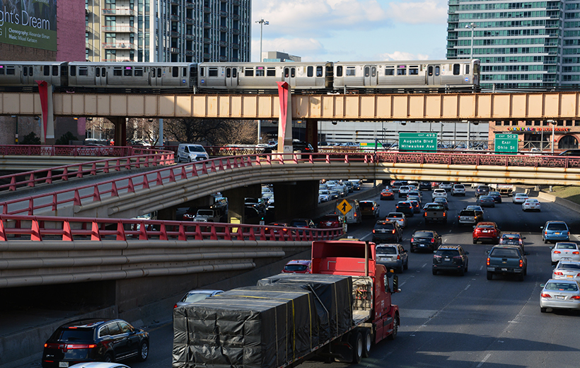 Various vehicles on I-90, the Kennedy Expressway, with a CTA elevated train passing overhead on bridge