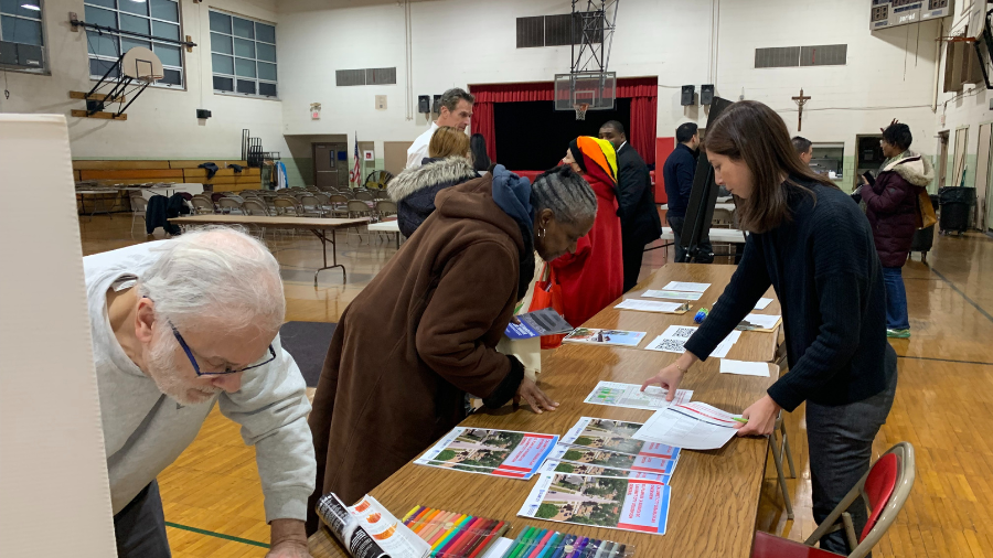 Woman stands on one side of a table and looks at a piece of paper a woman on the other side points to.
