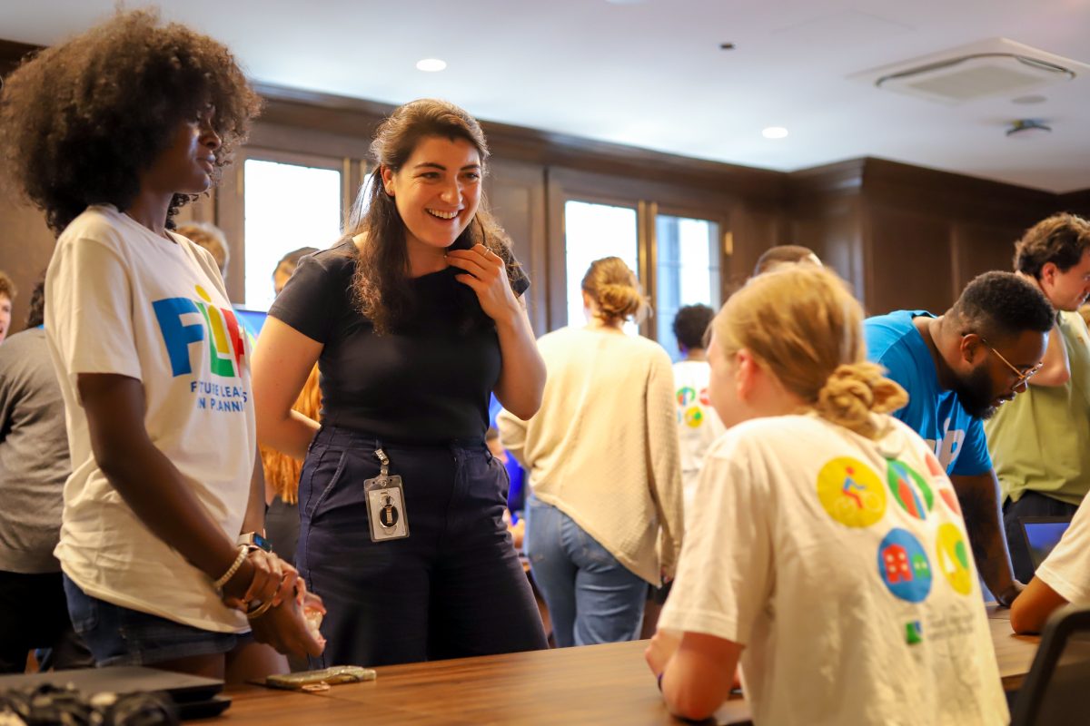 FLIP student and CMAP employee talk to another FLIP student who is sitting behind a desk. Lots of other people are behind them talking to others