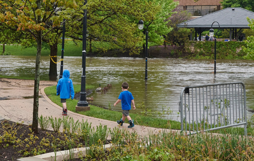 Two kids walk along flooded riverwalk. Lamp posts stick out of the water due to flooding