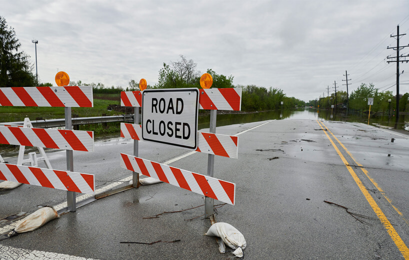 Road-closed signs and barriers with a flooded road in the background