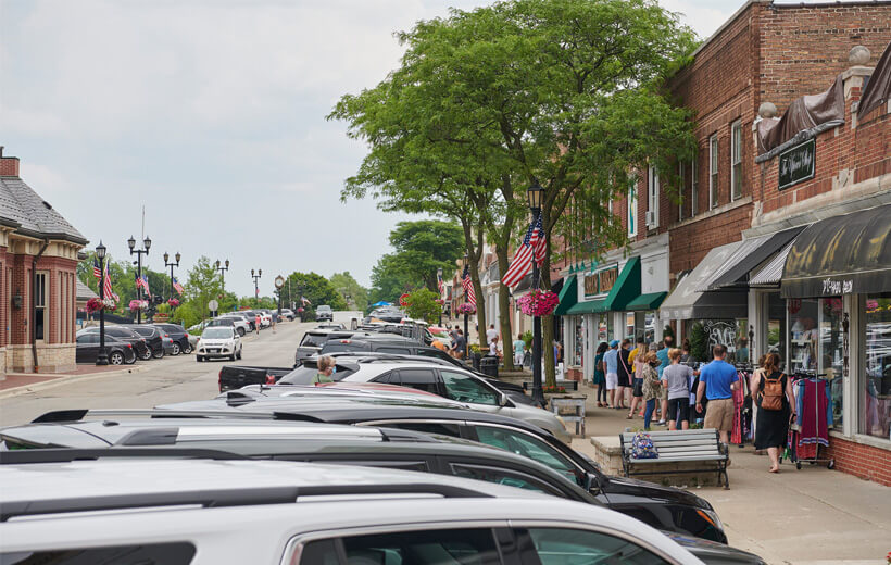 People on the sidewalk looking at stores and people lining up outside of a market.