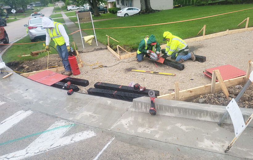 Construction crew installing ADA warning pads to the sidewalk crossing