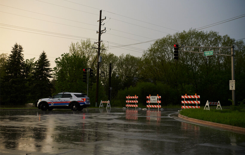 A police vehicle stationed by a barricade and road closure sign amidst rainy weather.