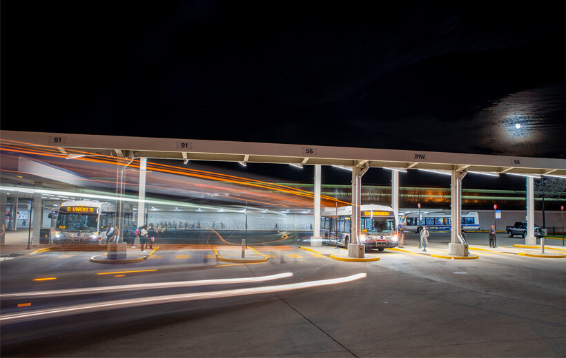 A nighttime scene at a bus and train station with buses and commuters on the move