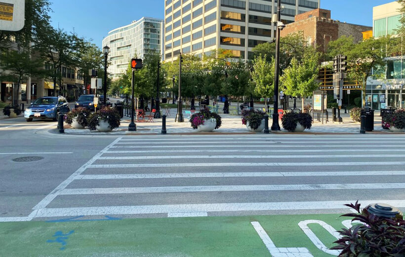A city crosswalk with a red hand signal indicating 'don't walk,' while cars wait at the traffic light on the left.