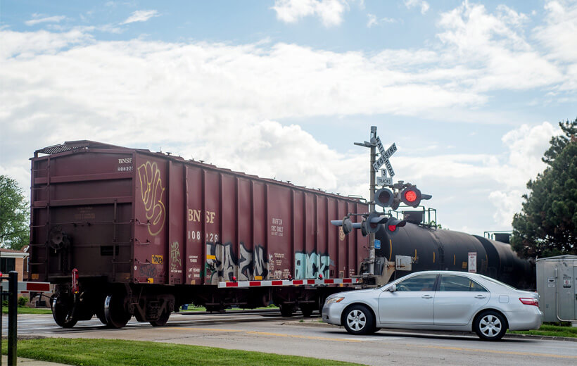 A car waiting at a rail road crossing as a train crosses.