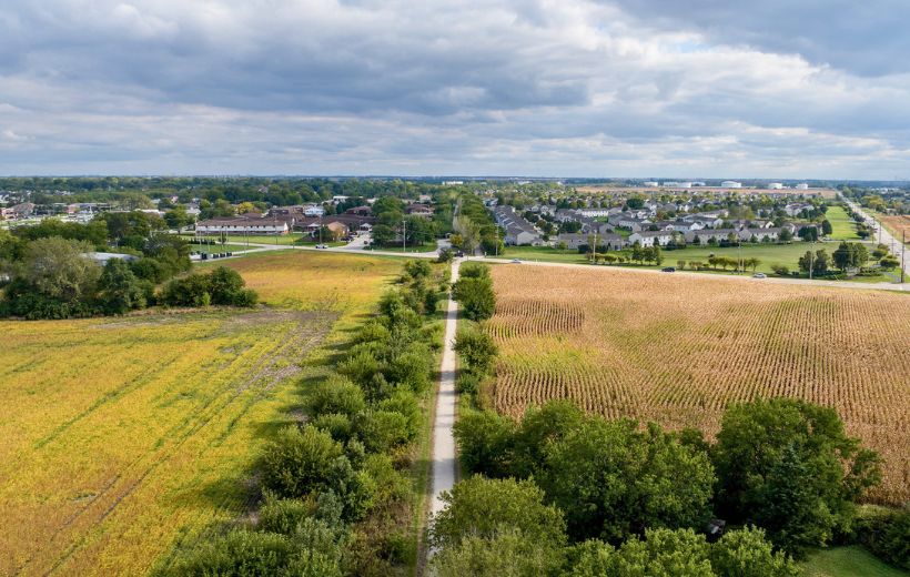Path through farm fields leading to area with housing and commercial buildings