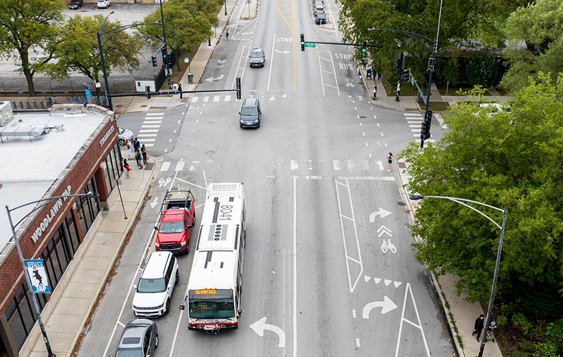Aerial photo of road with sidewalks on either side. Cars and bus drive on road.