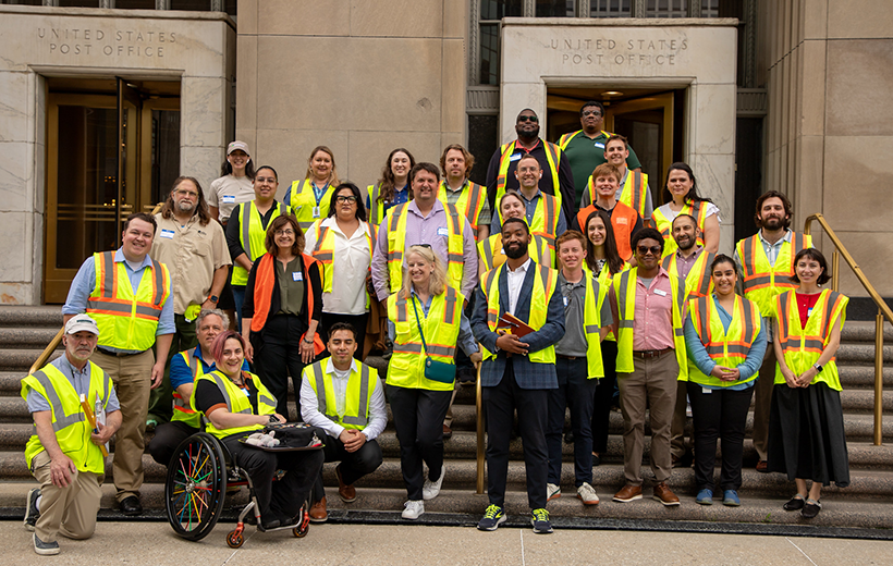 People in four rows smiling for group photo in front of the Chicago Old Post Office.