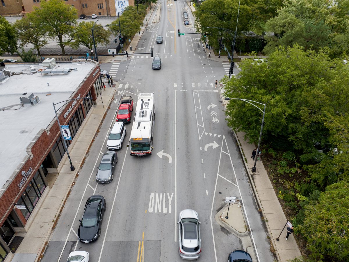 Aerial photo of road with sidewalks on either side. Cars and bus drive on road.